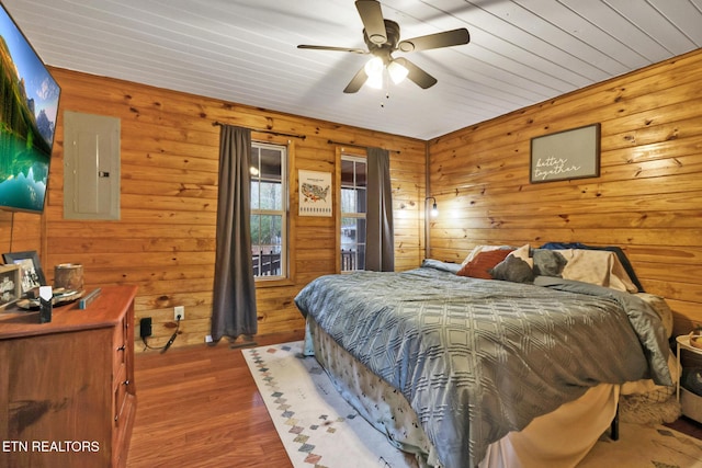 bedroom with hardwood / wood-style flooring, ceiling fan, wood walls, and electric panel