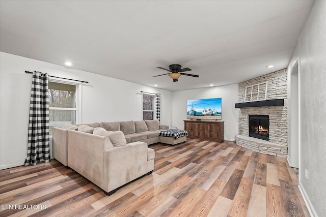 living room with a stone fireplace, ceiling fan, and wood-type flooring