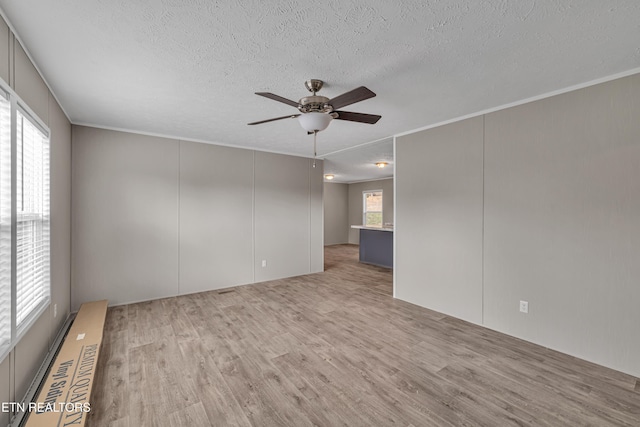 empty room with a wealth of natural light, light hardwood / wood-style flooring, ceiling fan, and a textured ceiling