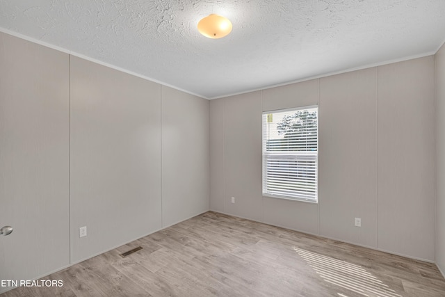 spare room with light hardwood / wood-style floors, ornamental molding, and a textured ceiling