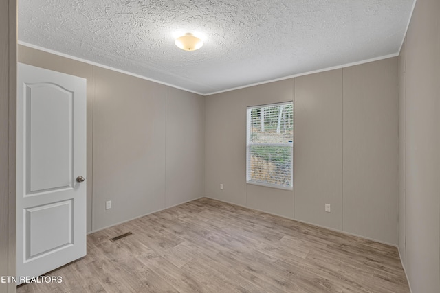 empty room with a textured ceiling, light hardwood / wood-style flooring, and ornamental molding