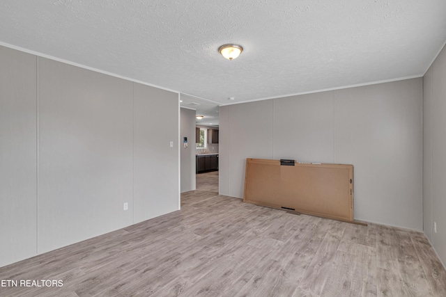 spare room with a textured ceiling, light hardwood / wood-style flooring, and crown molding