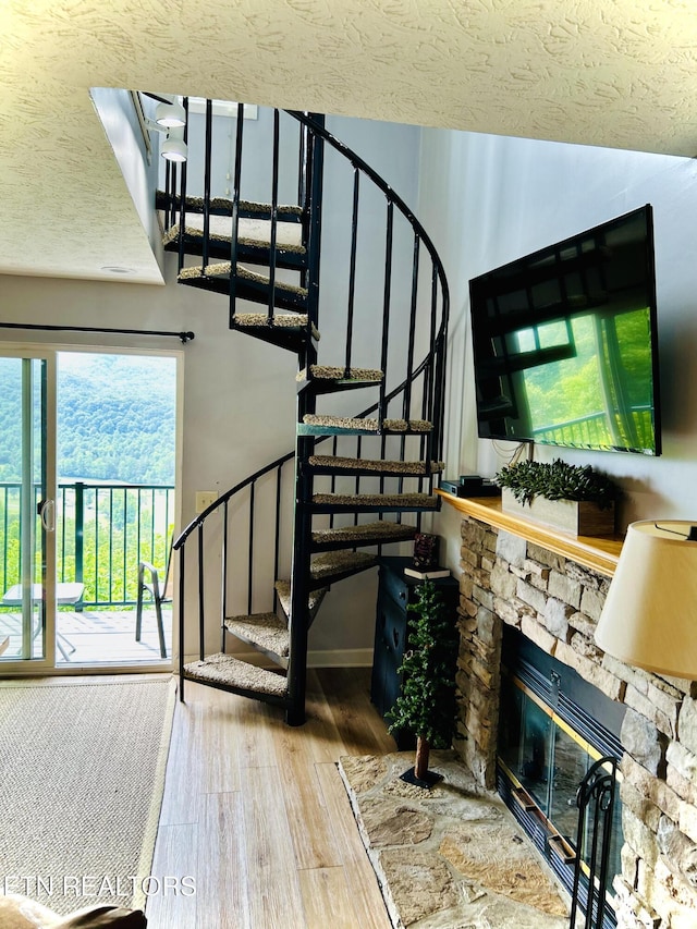 stairway with a stone fireplace, wood-type flooring, and a textured ceiling