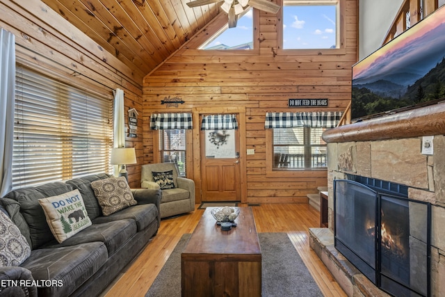 living room featuring high vaulted ceiling, wooden walls, a fireplace, wood ceiling, and light wood-type flooring