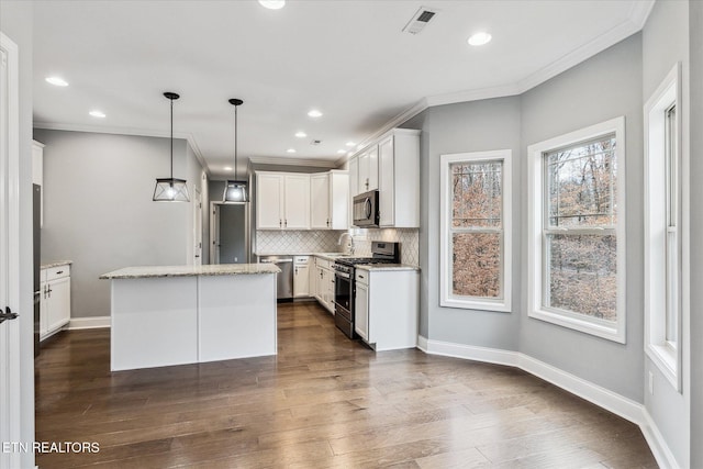 kitchen featuring hanging light fixtures, decorative backsplash, appliances with stainless steel finishes, a kitchen island, and white cabinetry