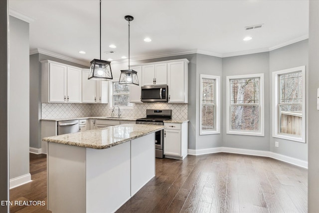 kitchen featuring appliances with stainless steel finishes, light stone counters, decorative light fixtures, a center island, and white cabinetry