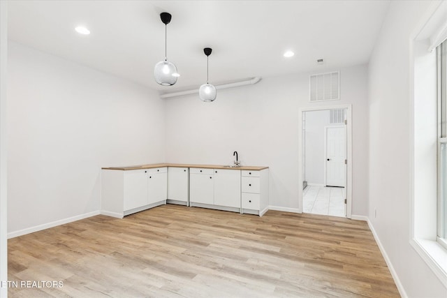 kitchen with white cabinets, decorative light fixtures, sink, and light hardwood / wood-style flooring