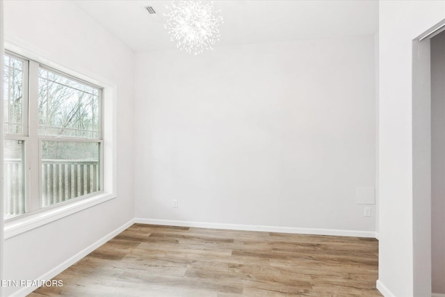 unfurnished room featuring a notable chandelier and light wood-type flooring