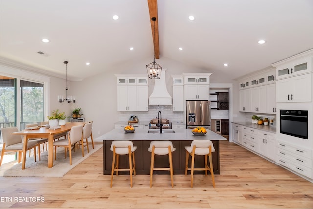 kitchen with a center island with sink, stainless steel fridge with ice dispenser, a sink, black oven, and tasteful backsplash