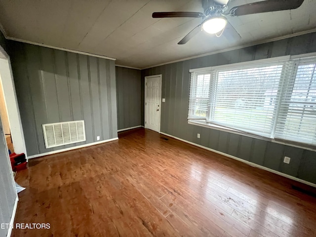 empty room with wood walls, ceiling fan, wood-type flooring, and ornamental molding