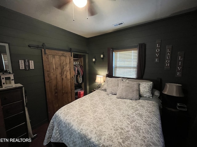 bedroom with a closet, a barn door, ceiling fan, and wood walls