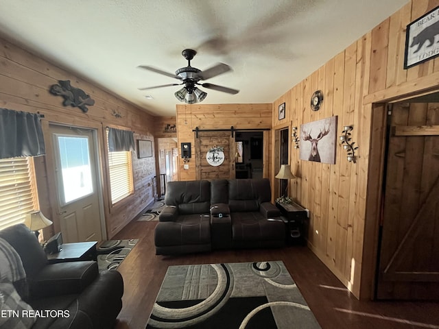 living room featuring ceiling fan, a barn door, dark hardwood / wood-style flooring, and wood walls