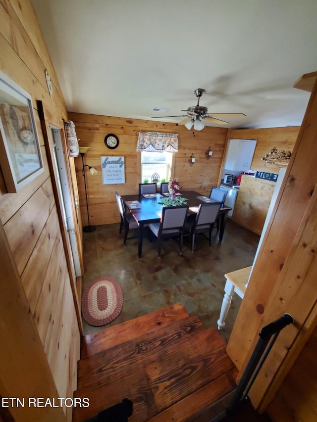 dining area with wooden walls and ceiling fan