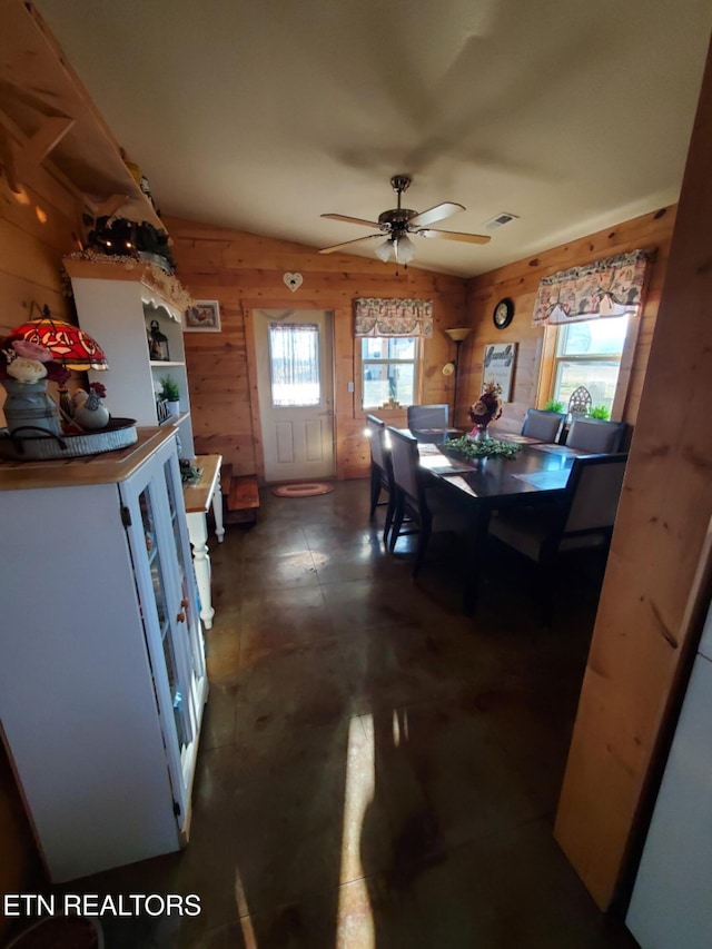 dining area featuring ceiling fan, a healthy amount of sunlight, and wood walls