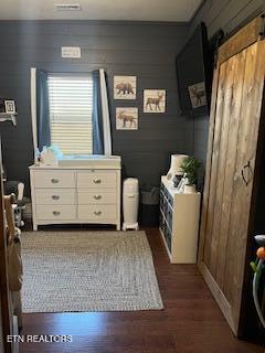 bedroom with dark wood-type flooring, a barn door, and wooden walls