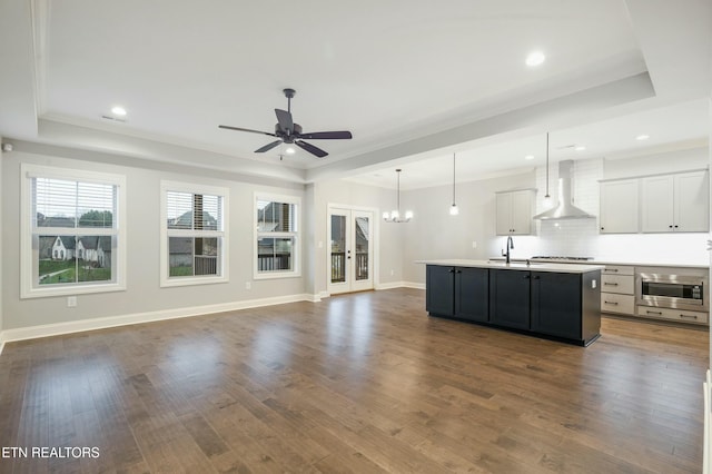 unfurnished living room with a raised ceiling, ceiling fan with notable chandelier, and dark hardwood / wood-style flooring