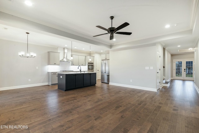 kitchen featuring a center island with sink, wall chimney range hood, hanging light fixtures, and appliances with stainless steel finishes