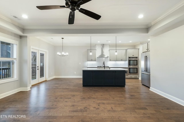 kitchen with french doors, white cabinets, a center island with sink, wall chimney range hood, and decorative light fixtures