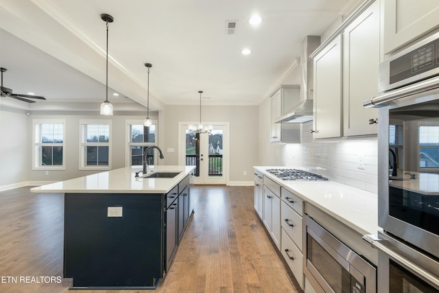 kitchen with sink, stainless steel appliances, pendant lighting, wood-type flooring, and a kitchen island with sink