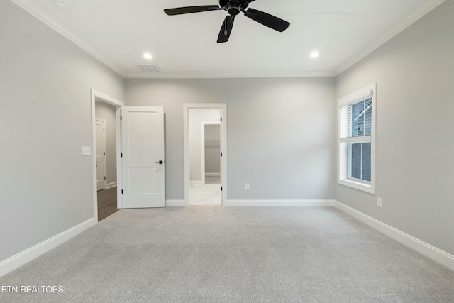 unfurnished bedroom featuring ceiling fan, a walk in closet, crown molding, and light carpet