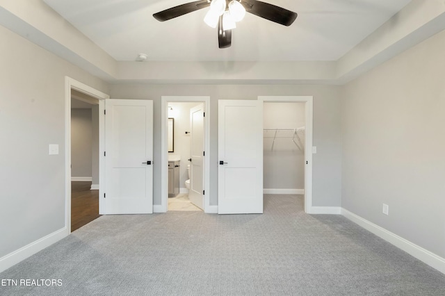 unfurnished bedroom with connected bathroom, ceiling fan, a spacious closet, light carpet, and a closet