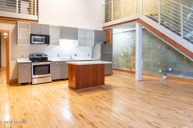 kitchen with appliances with stainless steel finishes, a towering ceiling, light wood-type flooring, a center island, and gray cabinets