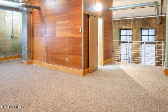 carpeted empty room featuring wooden walls