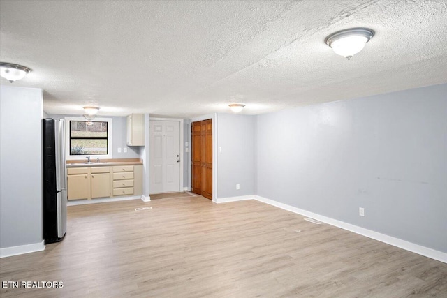 unfurnished living room featuring a textured ceiling, light wood-type flooring, and sink