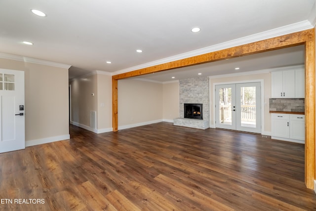 unfurnished living room featuring a fireplace, ornamental molding, dark wood-type flooring, and french doors