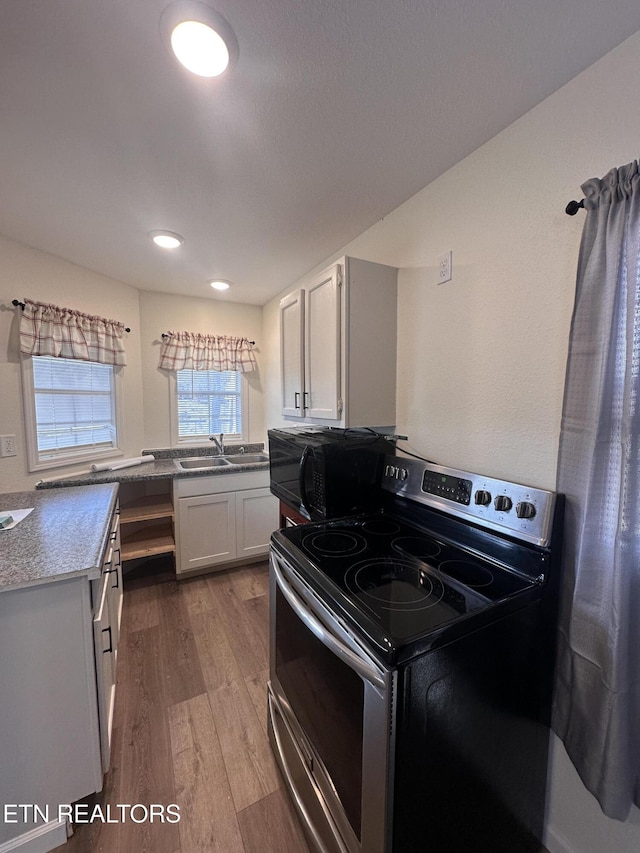 kitchen featuring stainless steel electric stove, sink, white cabinetry, and hardwood / wood-style floors