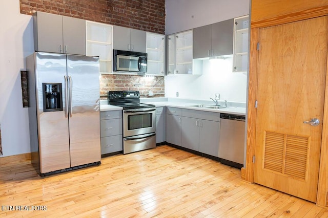 kitchen with stainless steel appliances, gray cabinets, light hardwood / wood-style floors, and brick wall