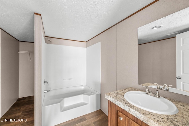 bathroom with vanity, a textured ceiling, crown molding, wood-type flooring, and washtub / shower combination