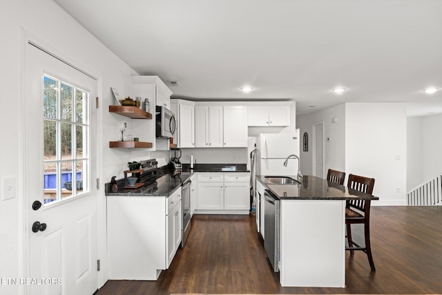 kitchen featuring stainless steel appliances, dark hardwood / wood-style flooring, a kitchen bar, a kitchen island with sink, and white cabinets