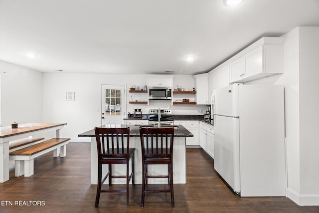 kitchen with white cabinets, stainless steel appliances, dark wood-type flooring, and an island with sink