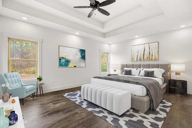 bedroom with baseboards, a tray ceiling, wood finished floors, and multiple windows