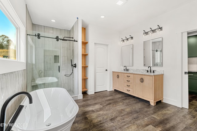 full bathroom featuring a stall shower, a sink, wood finished floors, a freestanding bath, and double vanity