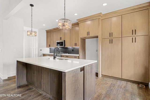 kitchen with light countertops, a sink, wood finished floors, stainless steel microwave, and decorative backsplash