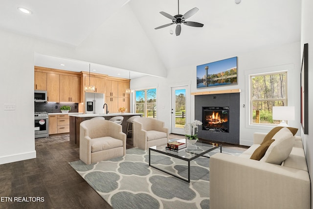 living area featuring a ceiling fan, a glass covered fireplace, dark wood-type flooring, and a wealth of natural light