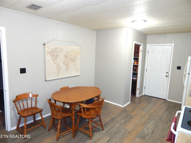 dining space featuring dark wood-type flooring and wooden walls