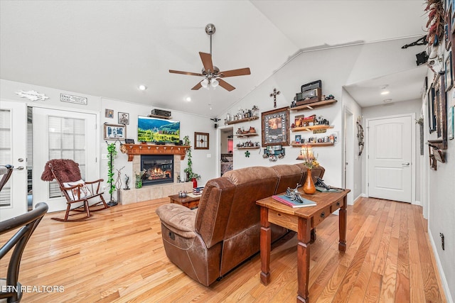 living room with ceiling fan, a tiled fireplace, light wood-type flooring, and vaulted ceiling