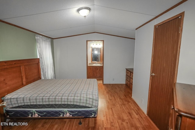 bedroom with ornamental molding, light wood-type flooring, ensuite bath, and lofted ceiling