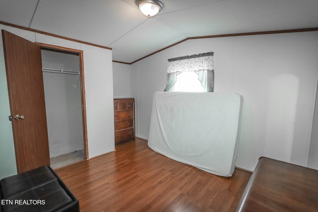 unfurnished bedroom with hardwood / wood-style flooring, lofted ceiling, crown molding, and a closet