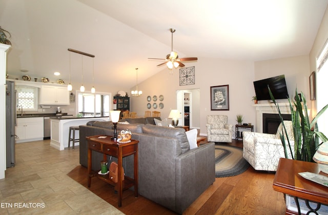 living room featuring light wood-style floors, a fireplace, vaulted ceiling, and ceiling fan with notable chandelier