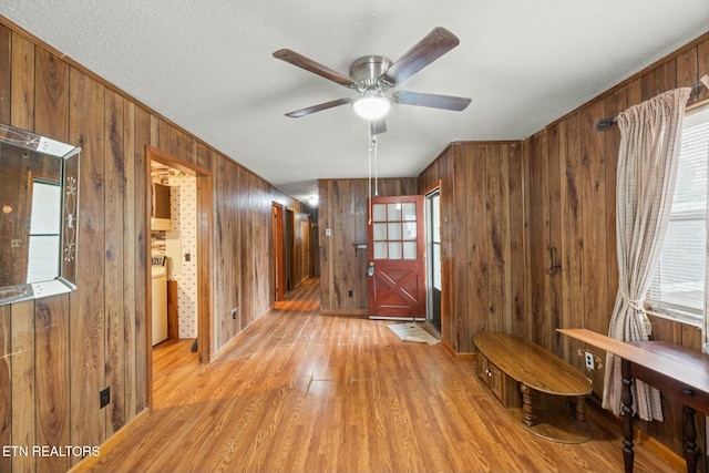 entrance foyer with a textured ceiling, ceiling fan, wooden walls, light hardwood / wood-style flooring, and washer / dryer