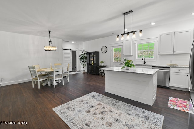 kitchen featuring a center island, stainless steel dishwasher, a barn door, decorative light fixtures, and white cabinetry