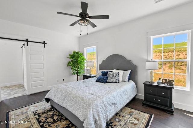 bedroom with a barn door, ceiling fan, and dark wood-type flooring