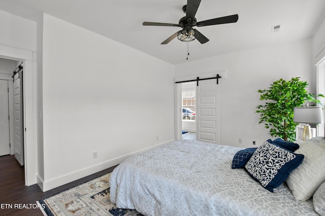 bedroom with ceiling fan, a barn door, and dark hardwood / wood-style flooring