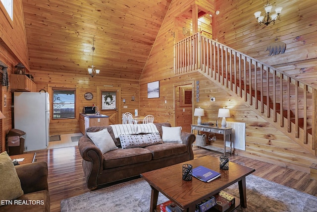 living room featuring light hardwood / wood-style flooring, high vaulted ceiling, a notable chandelier, and wood walls