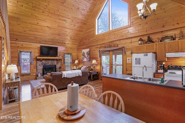 dining space with sink, an inviting chandelier, light hardwood / wood-style flooring, high vaulted ceiling, and wood walls