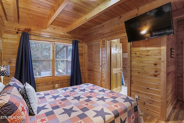 bedroom with beam ceiling, wooden ceiling, light hardwood / wood-style flooring, wooden walls, and a closet